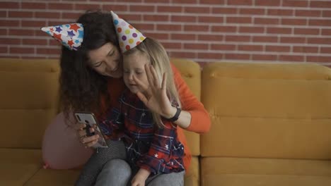 Mutter-Sitzt-Mit-Ihrer-Tochter-Im-Vorschulalter-In-Geburtstagsmützen-Und-Hat-Einen-Videoanruf-Per-Handy