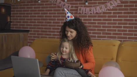 Mother-sitting-with-her-preschool-daughter-in-birthday-caps,-have-videocall-by-laptop