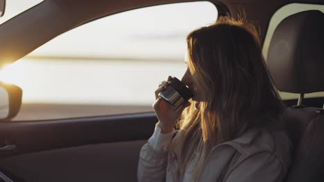 Woman-inside-the-car-is-drinking-coffee-from-the-thermos-cup,-adoring-sunrise
