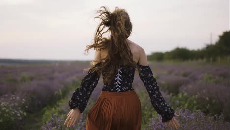 Long-haired-woman-running-joyfully-through-a-lavender-field,-touching-flowers
