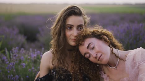 Portrait-of-two-curly-women-sitting-among-a-lavender-field,-embracing