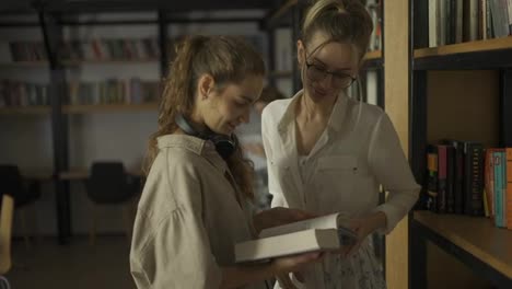Two-female-students-in-the-library-room-and-one-girl-showing-to-another-some-book