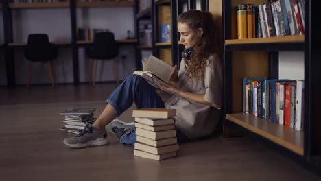 Nachdenkliche-Studentin-Sitzt-Vor-Einem-Bücherregal-Und-Hat-Bücher-Auf-Dem-Boden