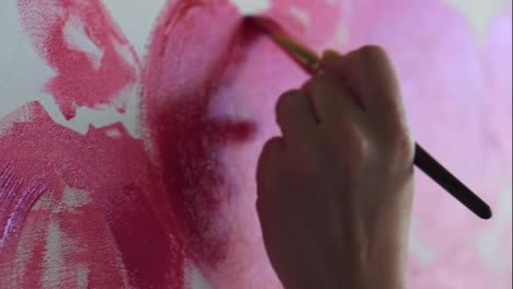 Close-up-of-unrecognizable-artist-paints-red-peonies-or-other-flowers-with-brush-on-the-canvas.-The-artist-paints-pink-flowers-on-canvas-with-thick-brush,-close-up,-side-view.-Natural-sun-light-lying-on-picture