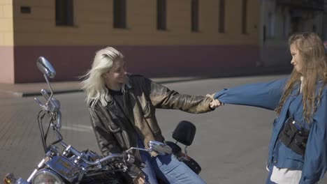 Two-young-women-in-love-and-mounted-motorcycle-in-the-city,-having-fun-together