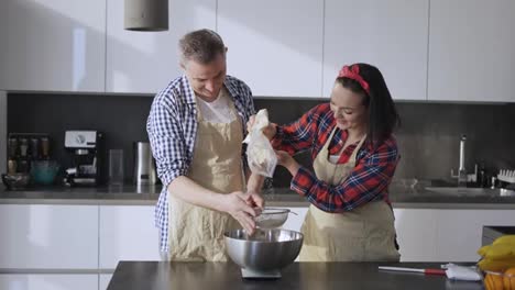 Portrait-of-a-couple-sifting-flour-to-make-bread-in-kitchen