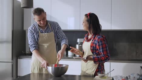 Young-man-preparing-food-and-woman-showing-him-something-in-recipe-book