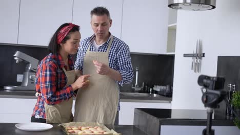 Adult-couple-at-kitchen-baking-at-home,-talking-on-camera-and-tasting-cookies