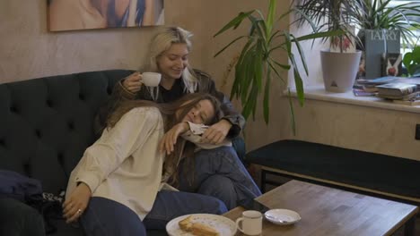 Happy-lesbian-lgbtq-couple-in-love-cuddling,-laughing,-drinking-coffee,-having-fun-relaxing-on-couch-at-cafe