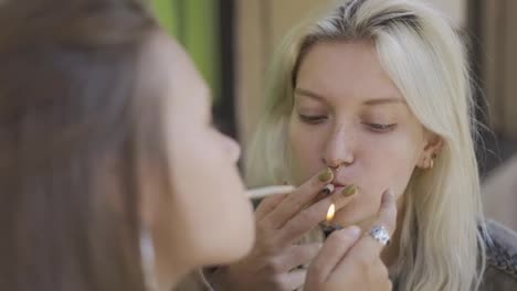 Two-girls-lighting-their-hand-rolled-cigarette,-enjoying-a-smoking-outside