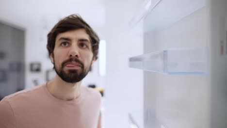 Man-opens-door-of-an-empty-fridge-surprised,-view-from-inside