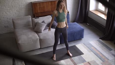 Tall-woman-doing-squat-exercise-on-yoga-mat-in-living-room-at-home-with-couch-on-the-background