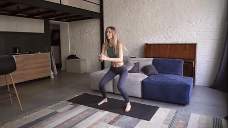 Dünne-Frau-Macht-Kniebeugenübungen-Auf-Einer-Yogamatte-Im-Heimischen-Wohnzimmer-Mit-Couch-Im-Hintergrund