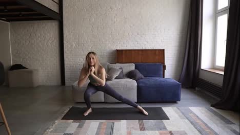 Frau-Macht-Side-Squat-Übungen-Auf-Einer-Yogamatte-Im-Heimischen-Wohnzimmer-Mit-Couch-Im-Hintergrund