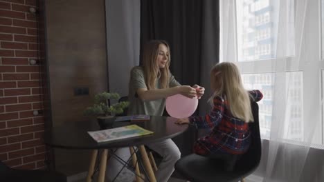 Little-girl-with-loving-mother-babysitter-inflates-blowing-air-balloon