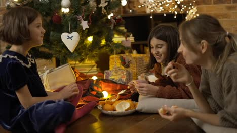 Mom-and-two-daughters-having-good-times-together,-eating-mandarines-under-Christmas-tree-at-home