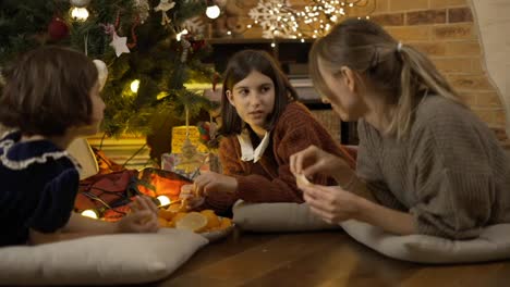Mom-and-two-daughters-having-good-times-together,-taking-mandarins-under-Christmas-and-talk