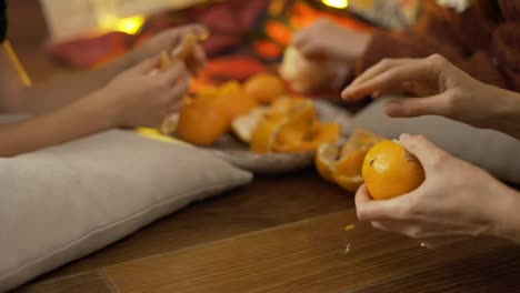 Close-up-of-hands,-family-taking-mandarins-under-Christmas-tree-in-lights