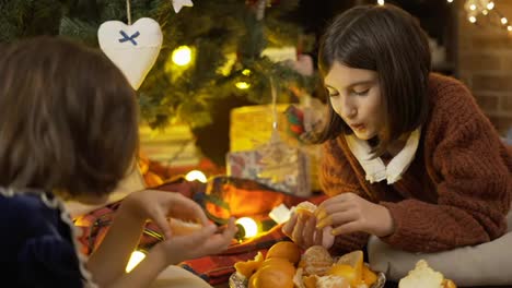 Two-little-girls-taking-mandarins-under-Christmas-tree-in-lights