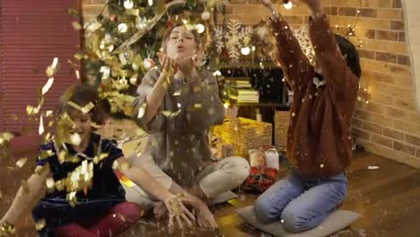 Mom-and-Daughters-catching-colored-confetti-in-hand-glad-laughing-near-Christmas-tree