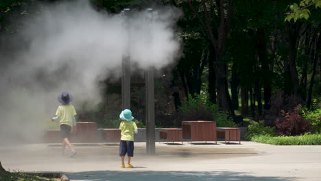 Niños-Jugando-Cerca-Del-Sistema-De-Pulverización-De-Agua-De-Refrigeración-Al-Aire-Libre-Con-Rociadores-De-Boquilla-En-El-Parque-Público-Yangjae-Foret-En-Seúl,-Corea-Del-Sur