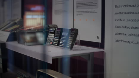 Computer-museum,-on-white-table-are-displayed-calculators,-behind-are-descriptions-and-their-history