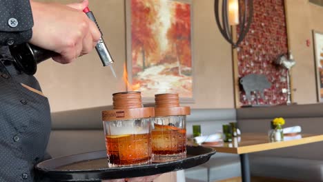 Bartender-flaming-hickory-smoke-infusion-into-high-end-whiskey-cocktail-drinks-with-fiery-blow-torch