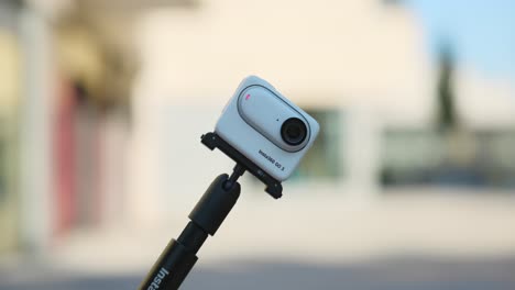Insta360-Go-3-On-Selfie-Stick-Coming-Into-Shot-With-Bright-Bokeh-Background