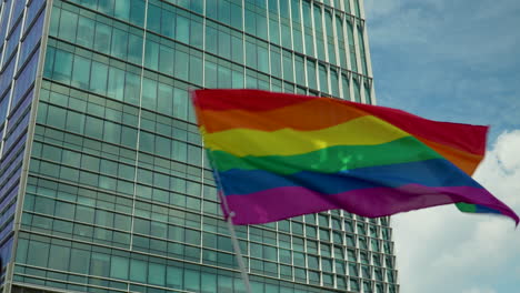 Colorful-pride-flag-waved-through-sky-in-front-of-skyscraper-in-Warsaw,-Poland