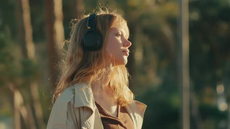 Young-woman-closes-eyes-listening-to-inspirational-podcast-outdoors-at-sunset