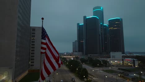 American-flag-waving-in-front-of-Renaissance-Center-and-General-Motor-Headquarters-in-Detroit,-Michigan