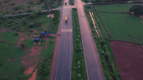 Tracking-Aerial-shot-of-a-goods-carrier-truck-on-a-Highway-road-through-farms-in-rural-Gwalior-of-India-during-Sunset-time