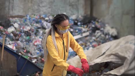 Woman-volunteer-in-yellow-and-transparent-protecting-glasses-sorting-used-plastic-bottles-at-modern-recycling-plant.-Separate