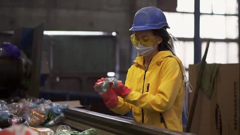 Woman-volunteer-in-yellow-and-transparent-protecting-glasses-and-mask-sorting-used-plastic-bottles-at-recycling-plant.-Separate-bottles-on-the-line,-removing-tops-and-squeeze-them