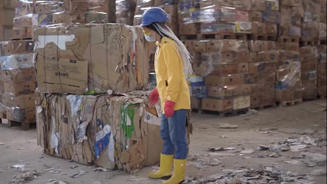 Unloading-of-waste-paper-in-a-warehouse-electric-car-controling-by-female-worker-in-hard-hat-and-yellow-jacket.-Huge-stocks-of-pressed-carton