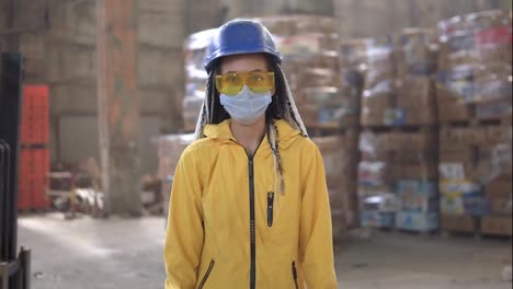 Waste-processing-plant.-Recycling-and-storage-of-waste-for-further-disposal.-Woman-worker-in-hard-hat,-gloves-and-mask-walking-through-the-stacks-of-pressed-disposal-waste,-huge-piles.-Front-view-footage.-Loading-machine-on-background