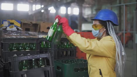 Woman-in-mask-working-at-the-recycle-waste-separation-of-recyclable-waste-plants.-Sorting-and-arranging-glass-bottles-into-boxes-for-further-disposal.-Slow-motion