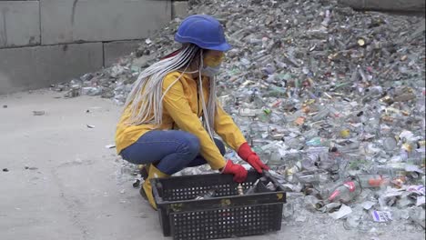 Woman-in-hard-hat-collecting-non-broken-white-glass-bottles-from-the-pile-of-broken-glass,-used-bottles-next-to-the-wall.-Girl-in-yellow-jacket-squatting-gathering-old-glass-bottles-for-further-recycling.-Slow-motion
