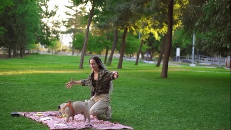 Woman-with-dreadlocks-playing-with-her-dog-on-grass,-having-picnic-outdoors-in-the-green-park-alone