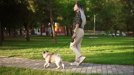 Purebred-pug-running-in-the-park-with-dreadlocks-female-owner-leading-the-leash-in-summer