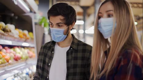 Young-couple-in-face-masks-shopping-for-fresh-produce-at-market