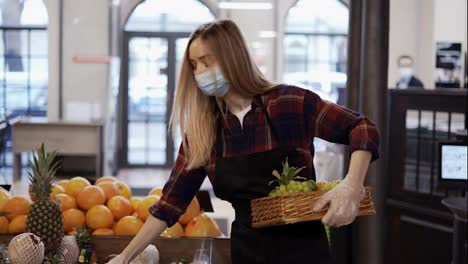 Female-worker-in-black-apron-and-mask-stocking-the-fruits-in-supermarket