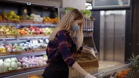Female-worker-in-black-apron-and-mask-stocking-fresh-avocados-in-supermarket