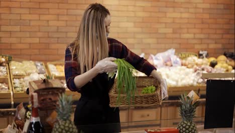 Female-worker-in-black-apron-and-mask-arranging-greens-in-supermarket