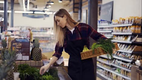 Female-worker-in-black-apron-arranging-greens-in-supermarket,-removing-spoiled