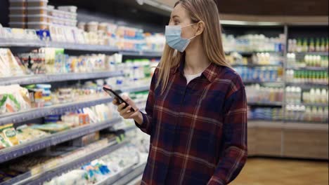 Woman-taking-milk-in-supermarket-using-smart-phone,-checking-shopping-list