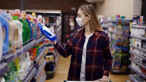 Woman-choosing-detergent-at-a-household-goods-in-the-store-in-mask