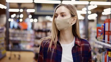 Mujer-Con-Máscara-Protectora-Caminando-Por-El-Supermercado-Entre-Pasillos,-Buscando-Algo