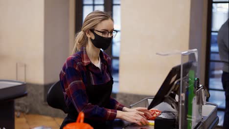 Female-cashier-in-a-protective-mask-and-gloves-pierces-the-products-with-the-scanner