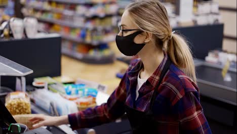 Female-cashier-in-a-protective-mask-pierces-the-products-with-the-scanner